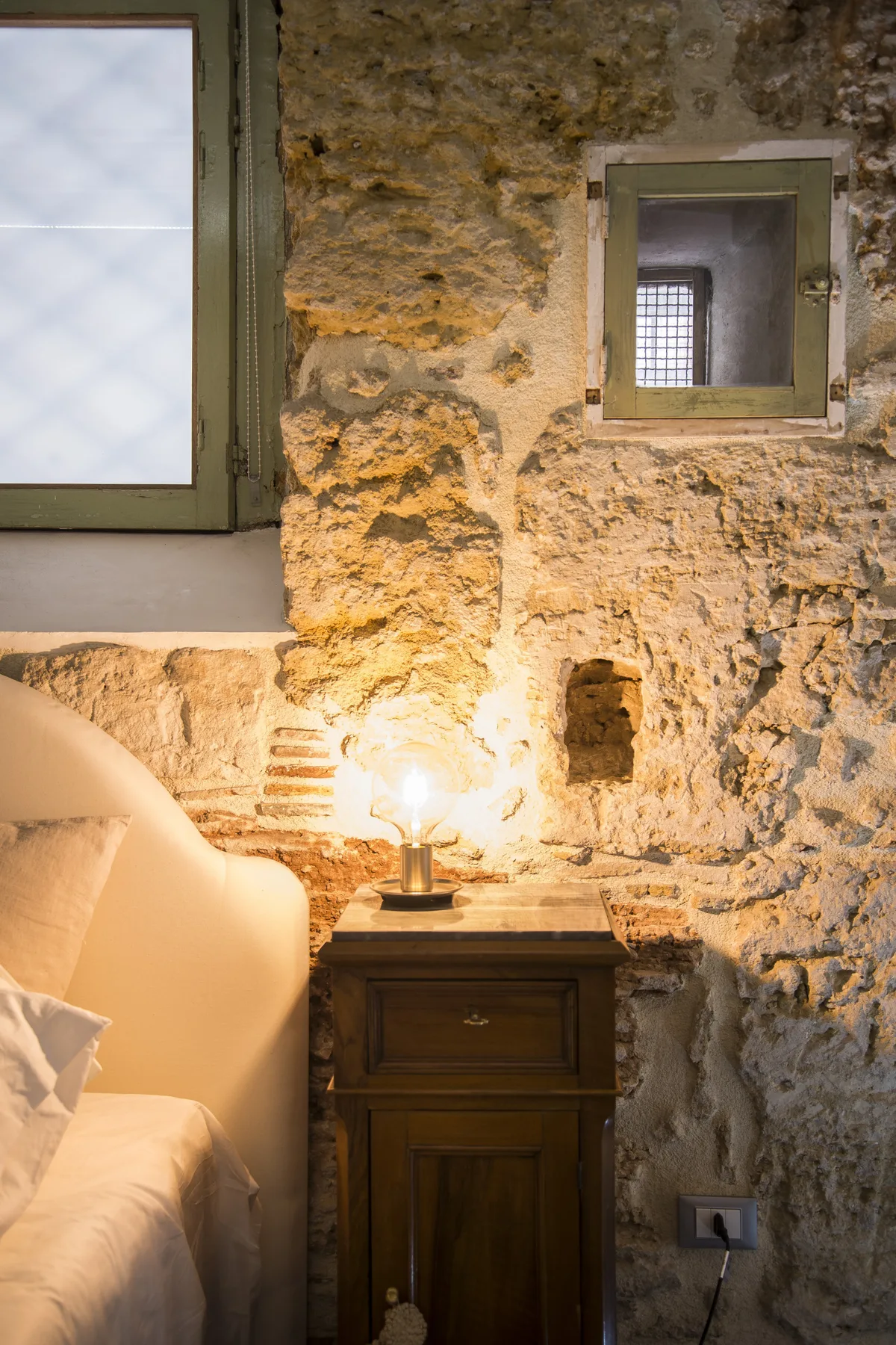 A bedroom with a bedside table beside a bed against a stone wall.