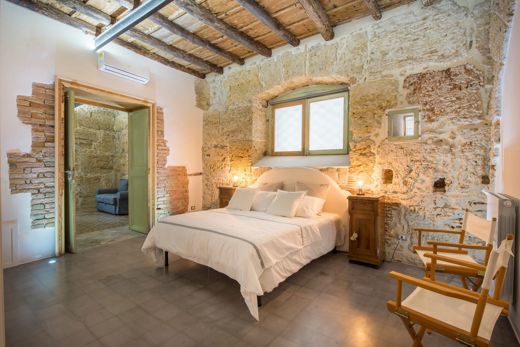 A bedroom with a bed beneath a window and exposed wooden ceiling beams.