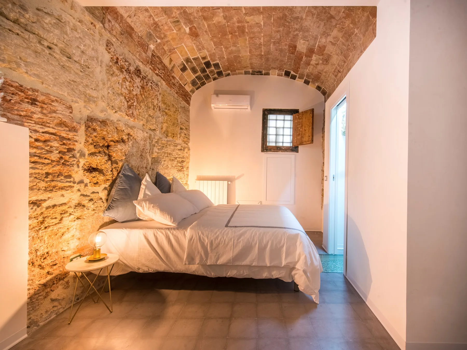 A bedroom with a neatly made bed beneath a curved brick ceiling.