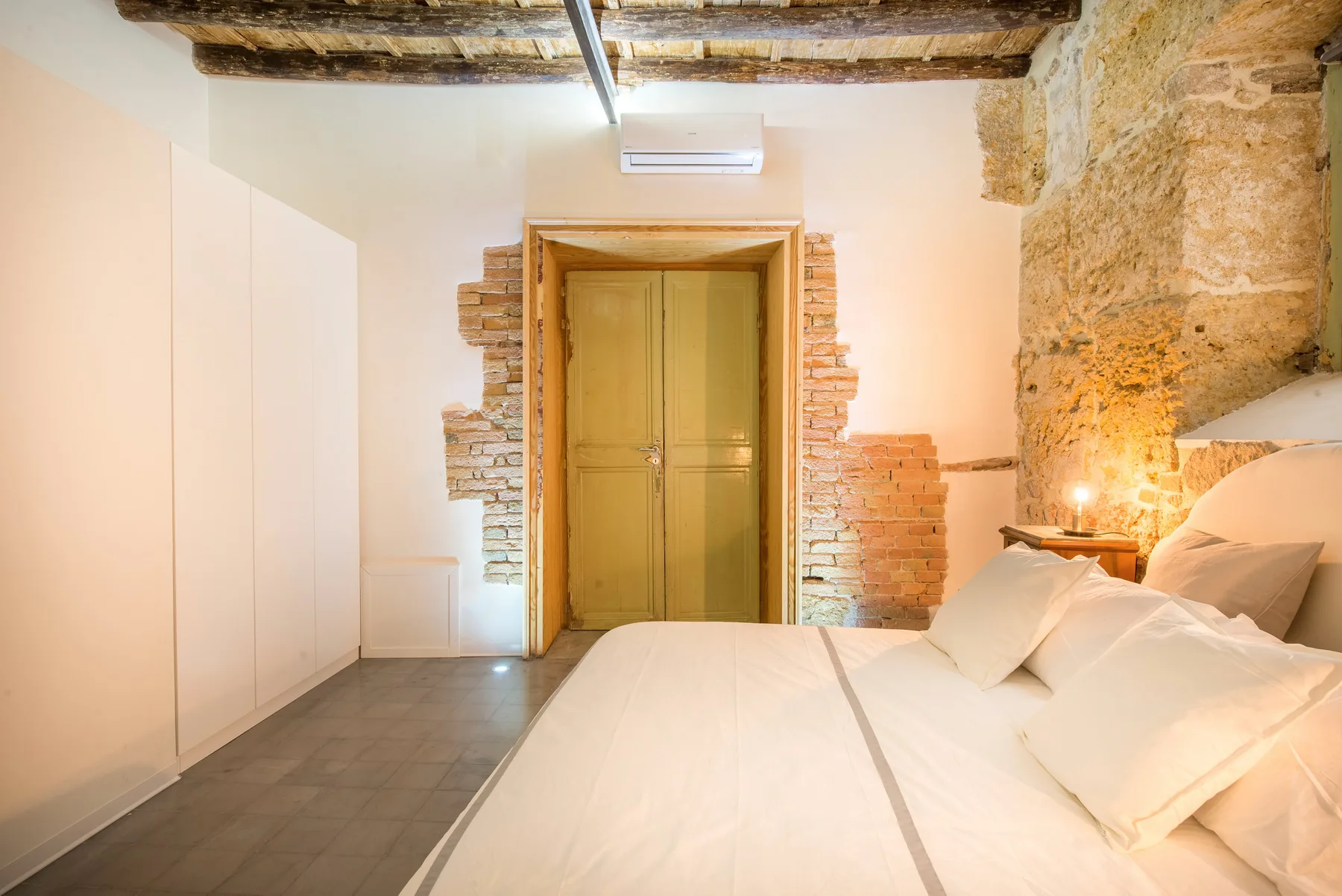 A bedroom with a double bed, white bedding, and exposed stone walls.