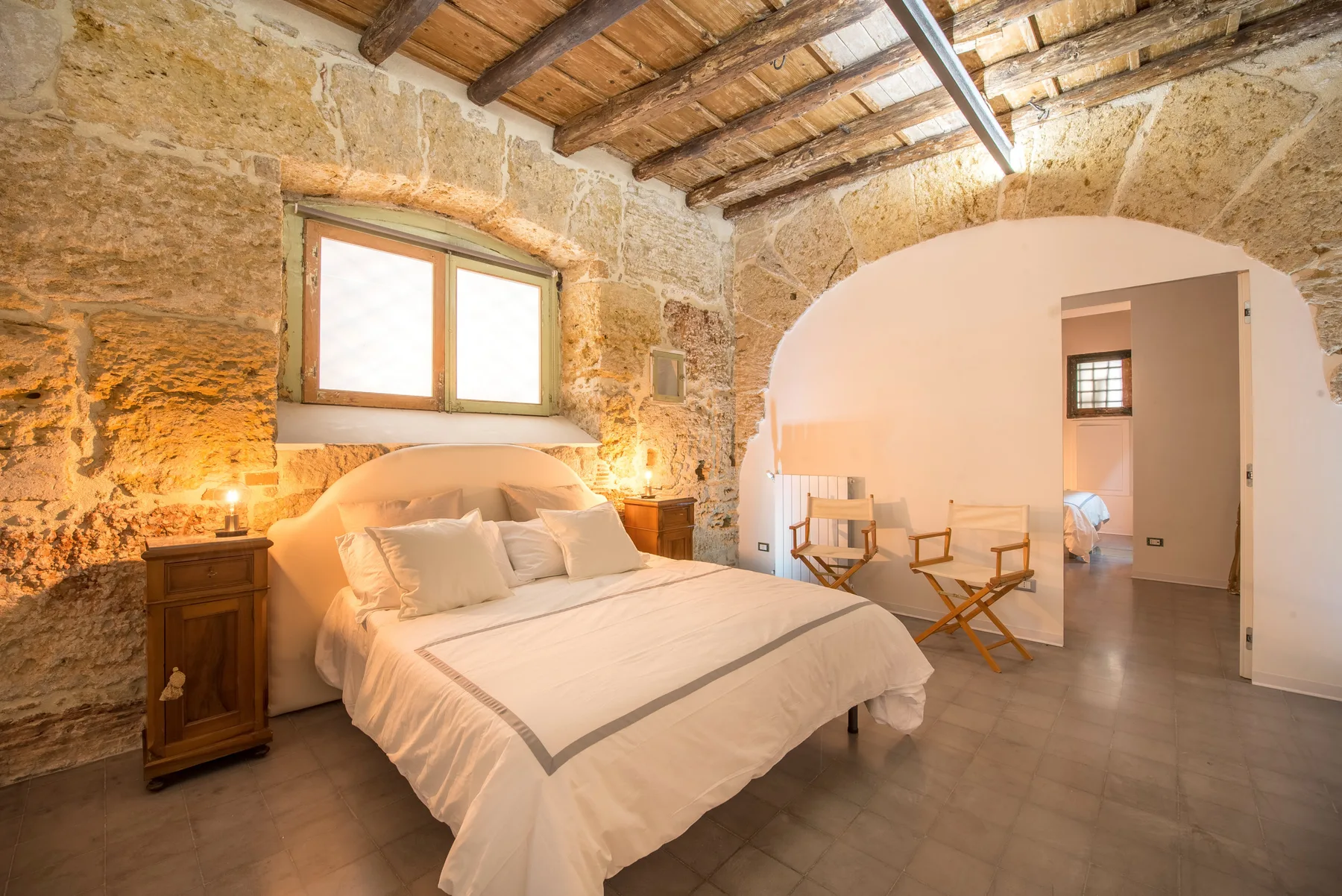 A bedroom with a bed beneath a window and exposed wooden ceiling beams.