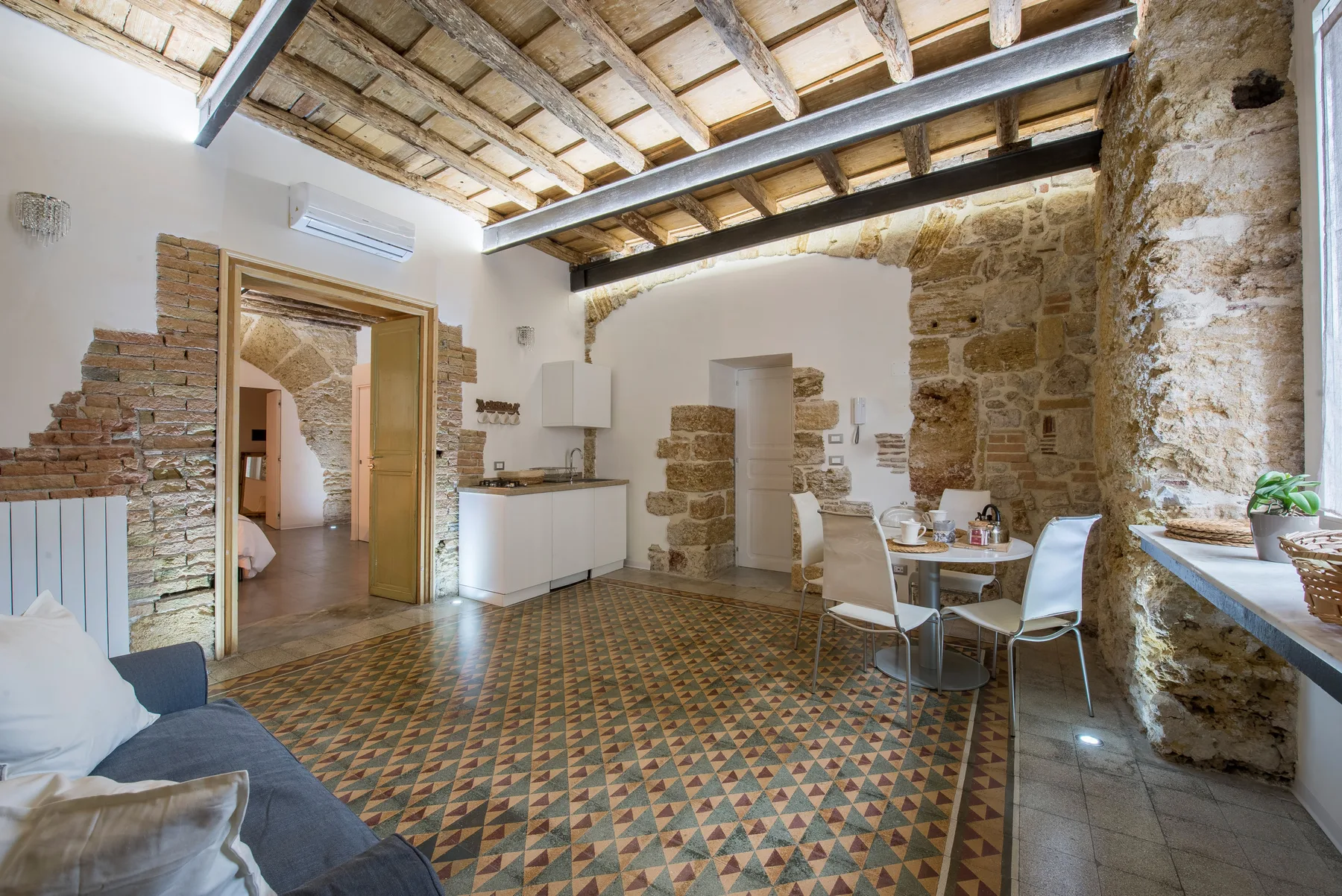 A rustic dining and kitchen area with exposed beams and patterned tile flooring.
