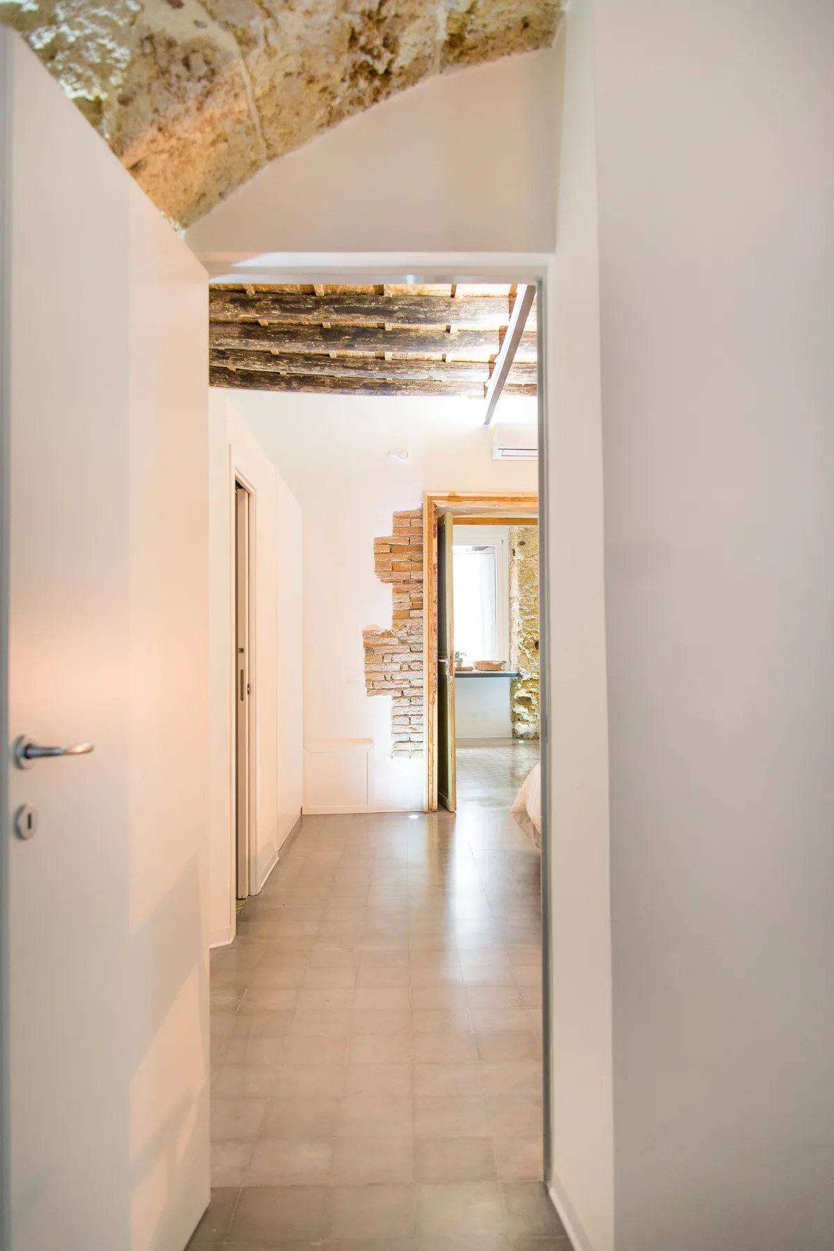 A bright interior hallway with tiled flooring and an exposed brick section.