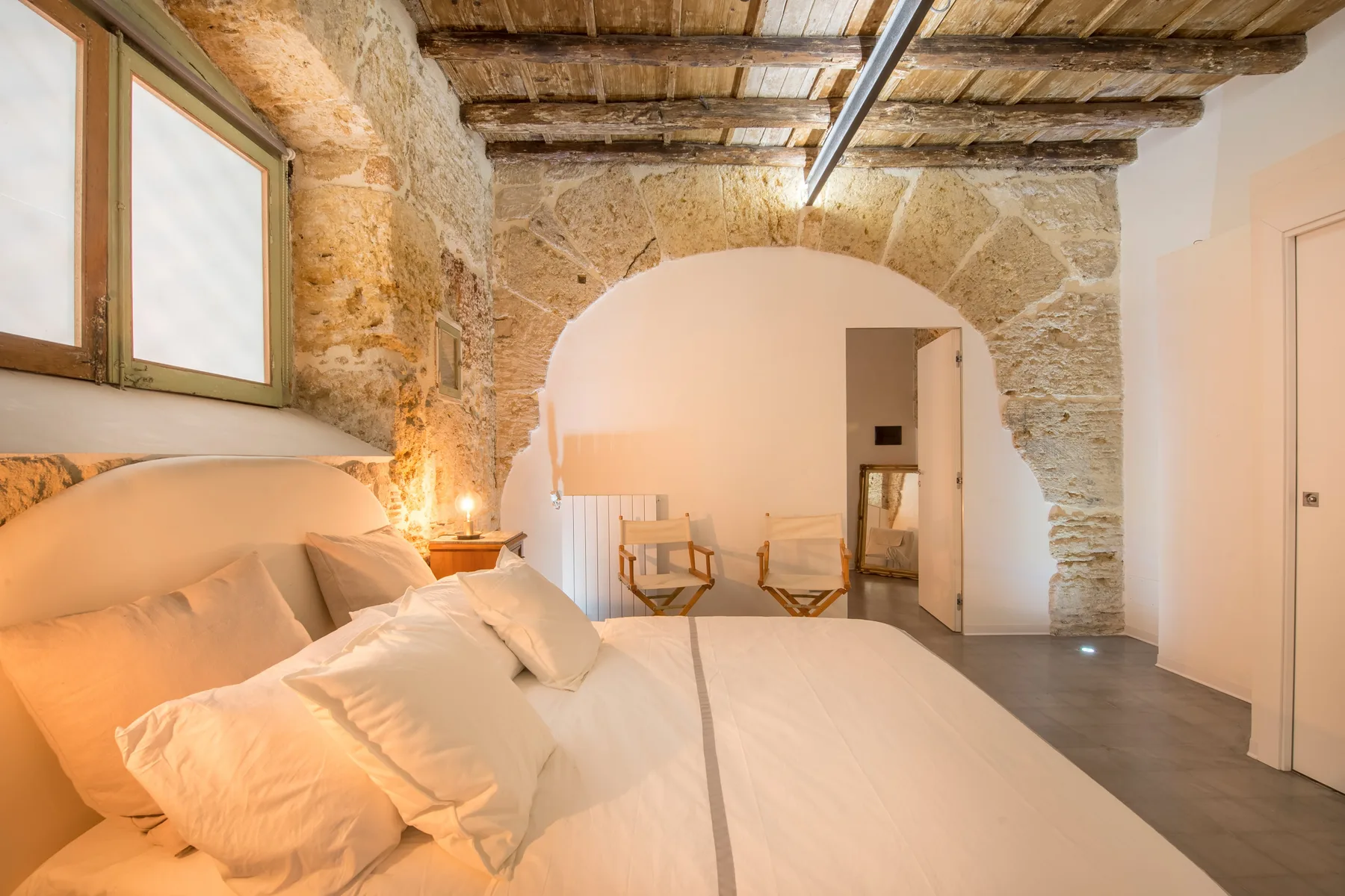 A bedroom with a large bed beneath exposed wooden ceiling beams.