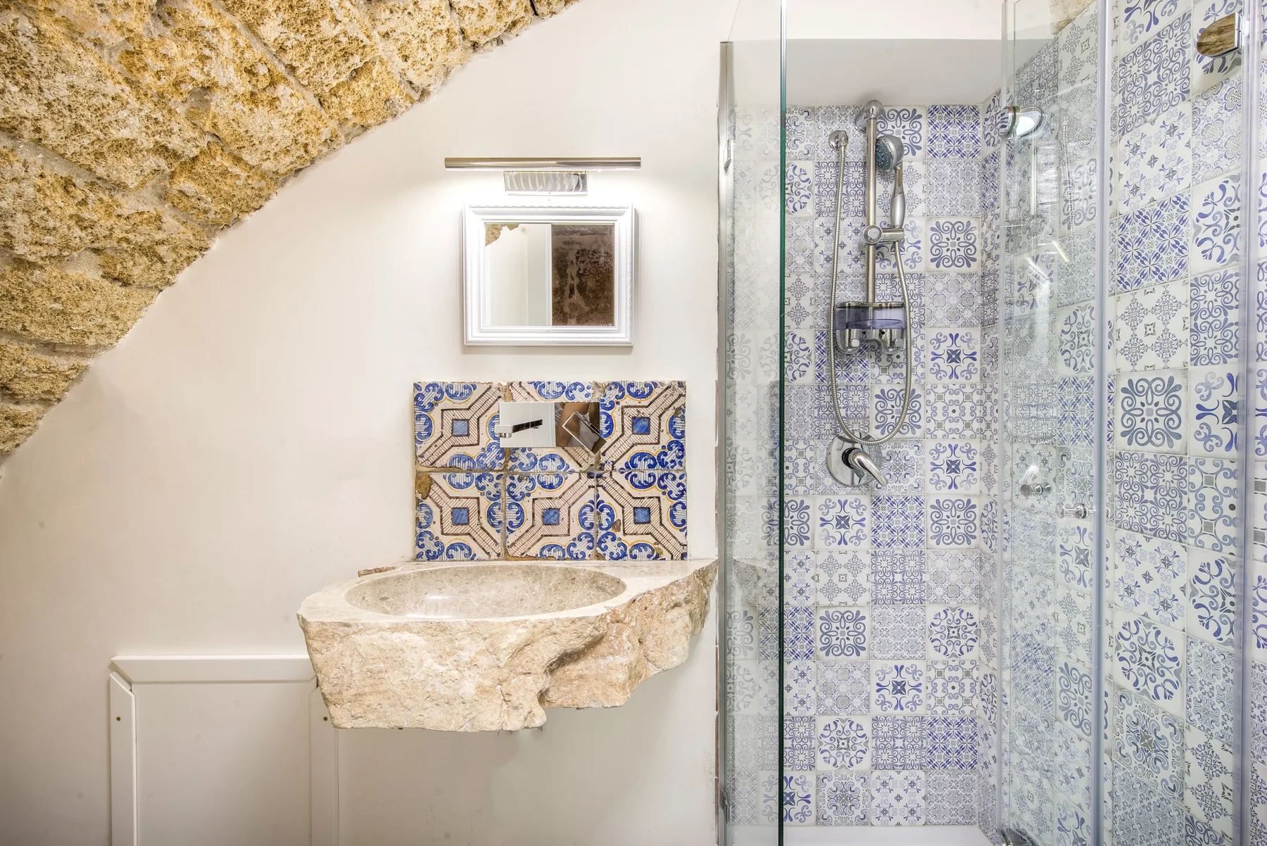 A bathroom with a stone sink beside a glass shower lined with patterned tiles.