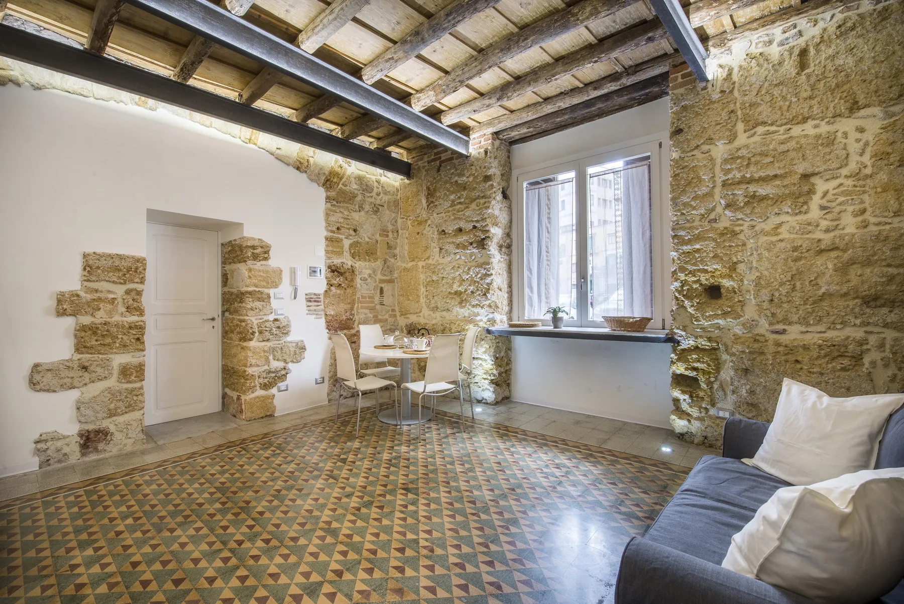 A rustic living room with exposed stone walls, patterned tile flooring, and a seating area.