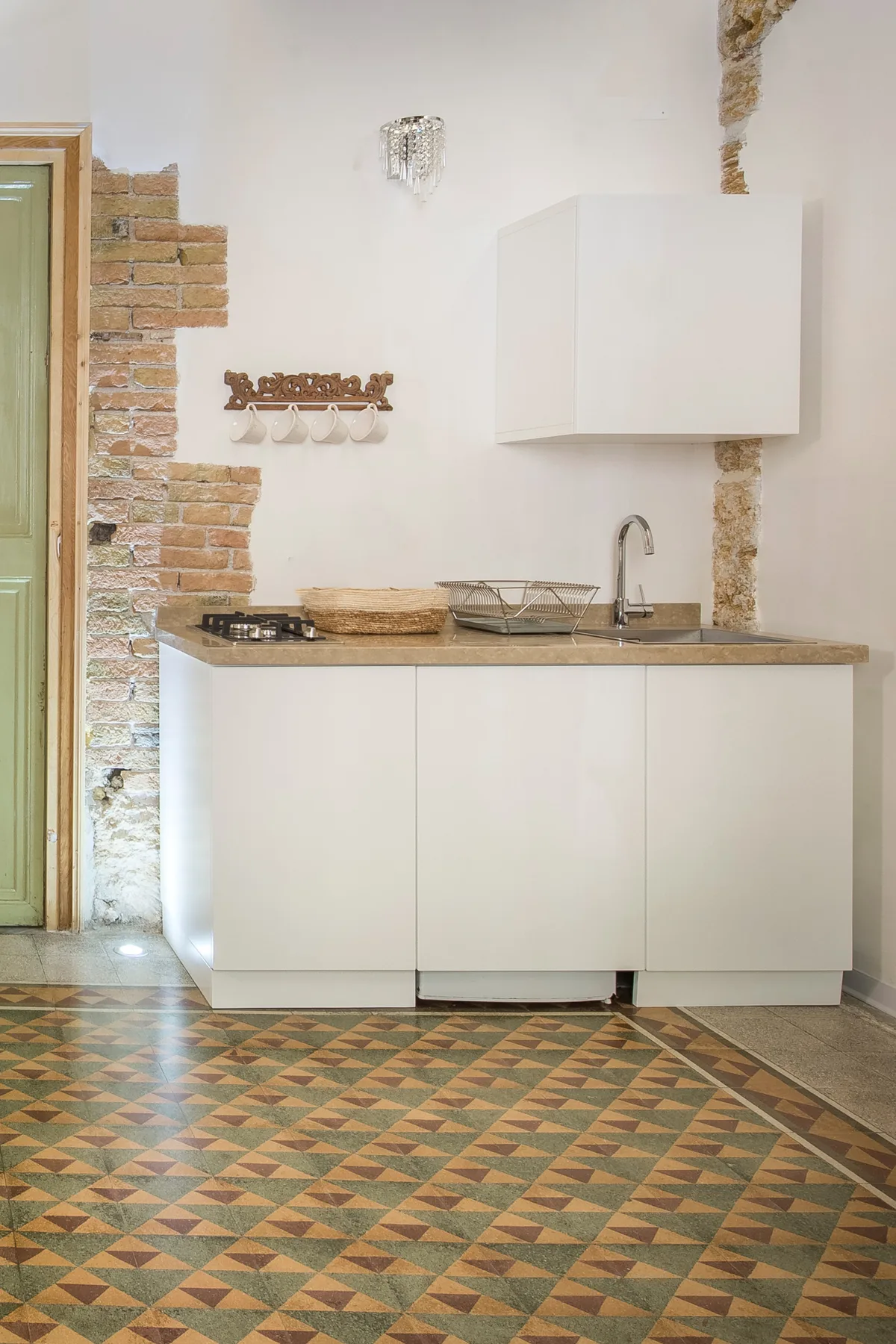 A compact kitchen with white cabinets, a countertop, and patterned floor tiles.