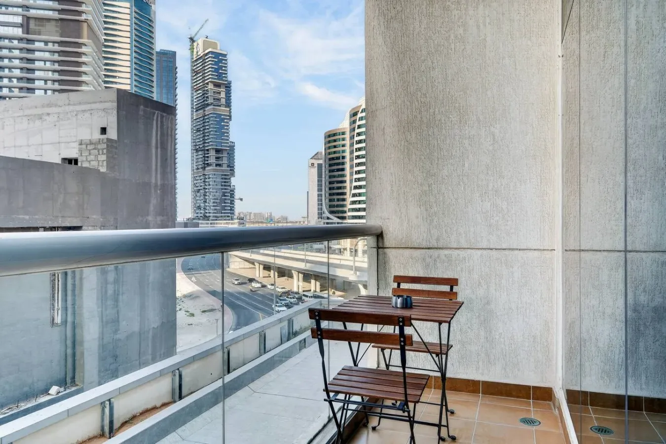 A balcony with a small table and seating overlooks nearby city buildings.