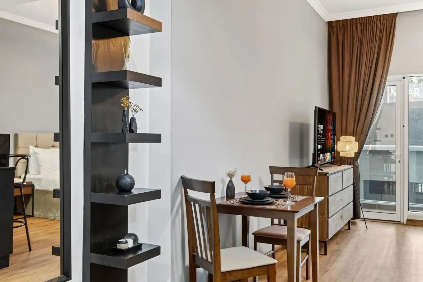 Comedor con mesa y sillas junto a un televisor y puertas de vidrio con cortinas.
