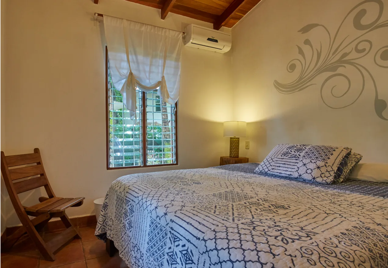 Habitación triple con ropa de cama estampada, una silla y aire acondicionado.