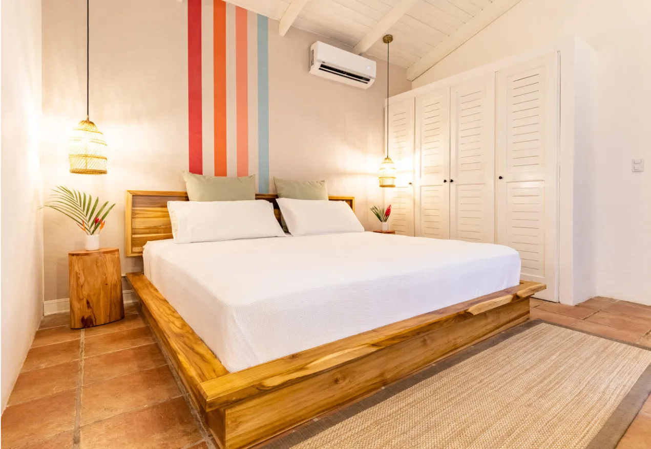 Habitación superior con cama king de madera, una pared decorativa a rayas y puertas de armario con lamas.
