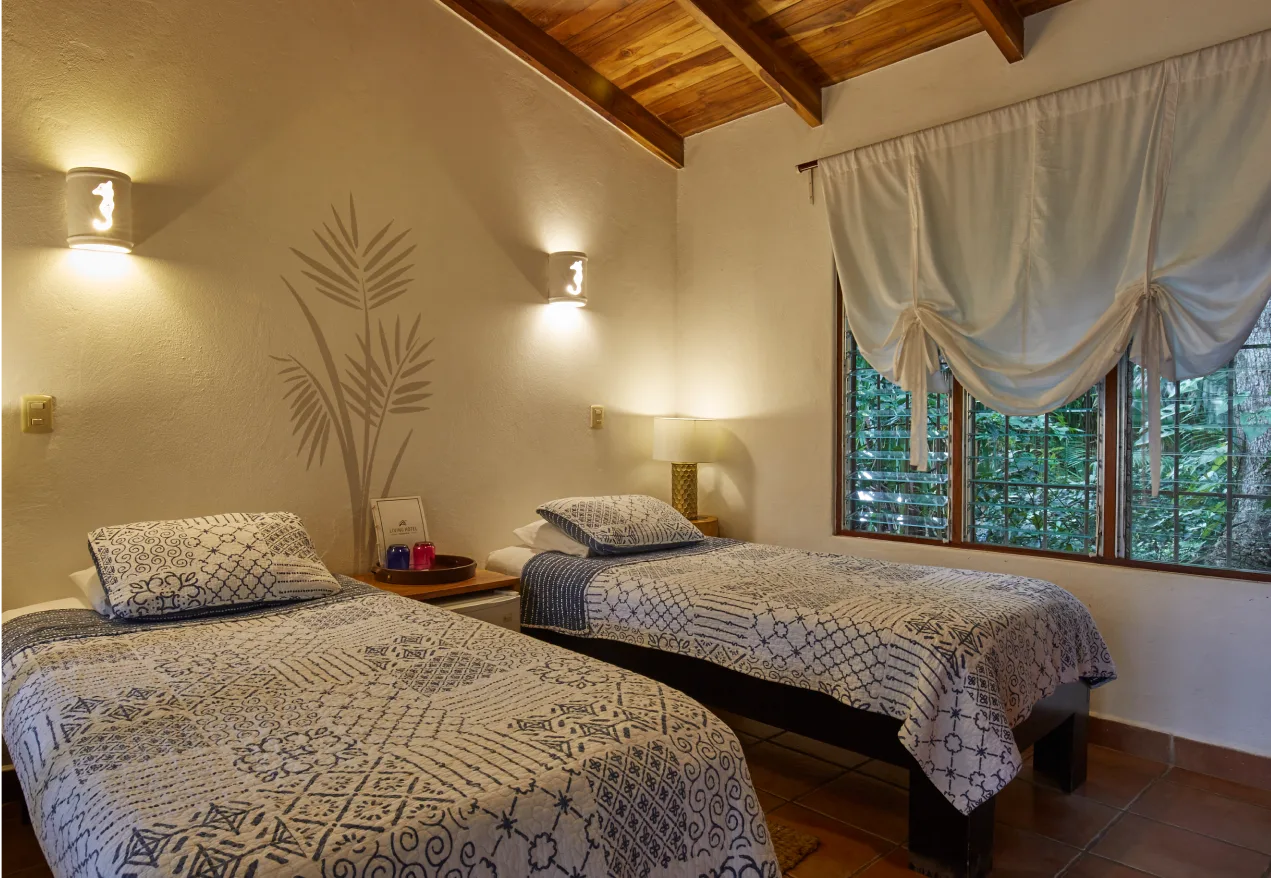 Habitación con dos camas individuales y un mural de hojas de palmera en la pared.