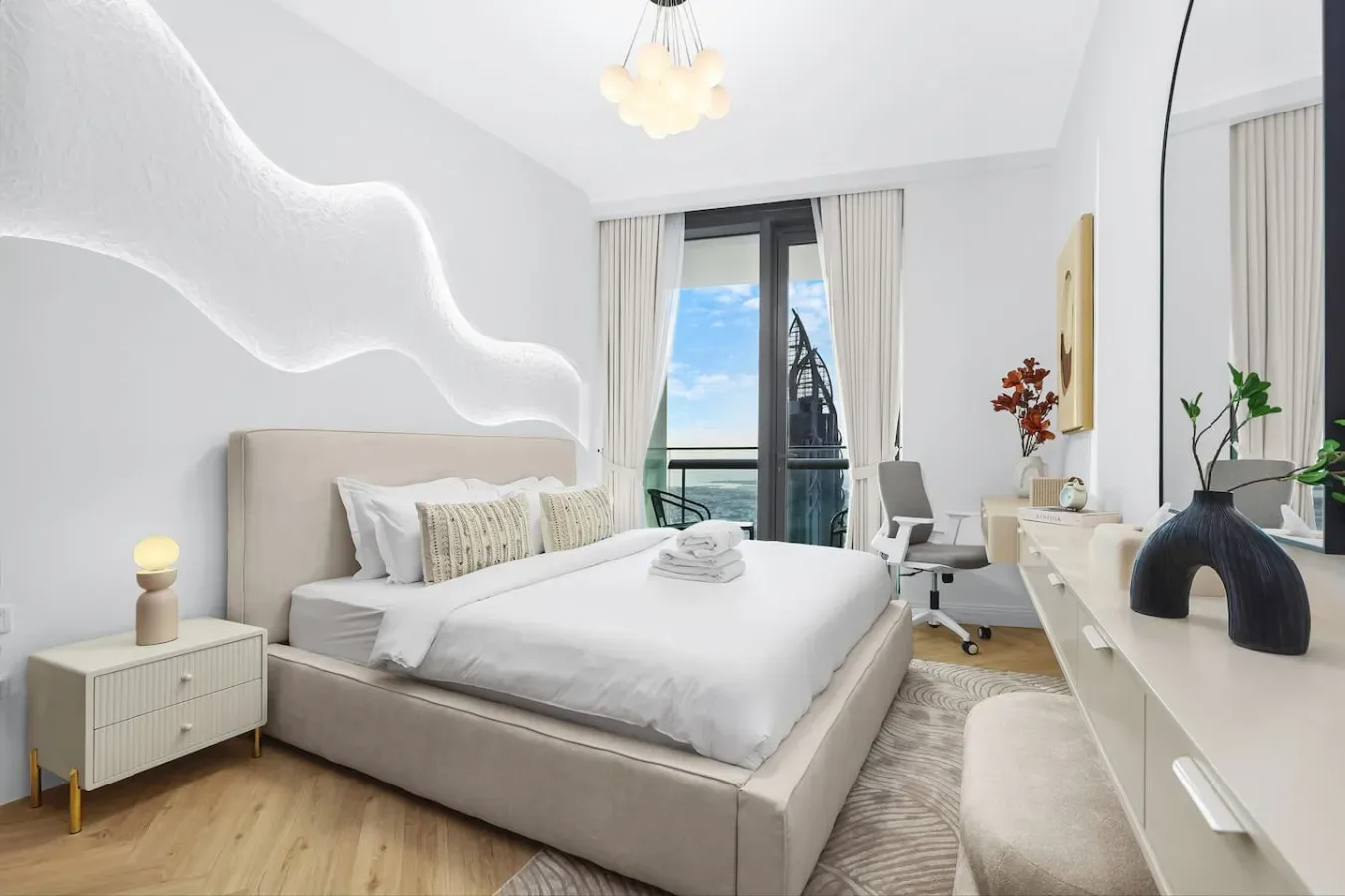 A bright bedroom with a neatly made bed and a glass door opening to a balcony.