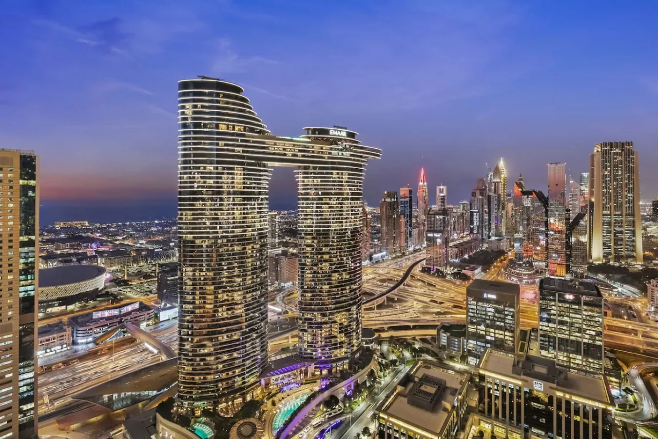 A city skyline at dusk, with illuminated high-rise buildings and roads.