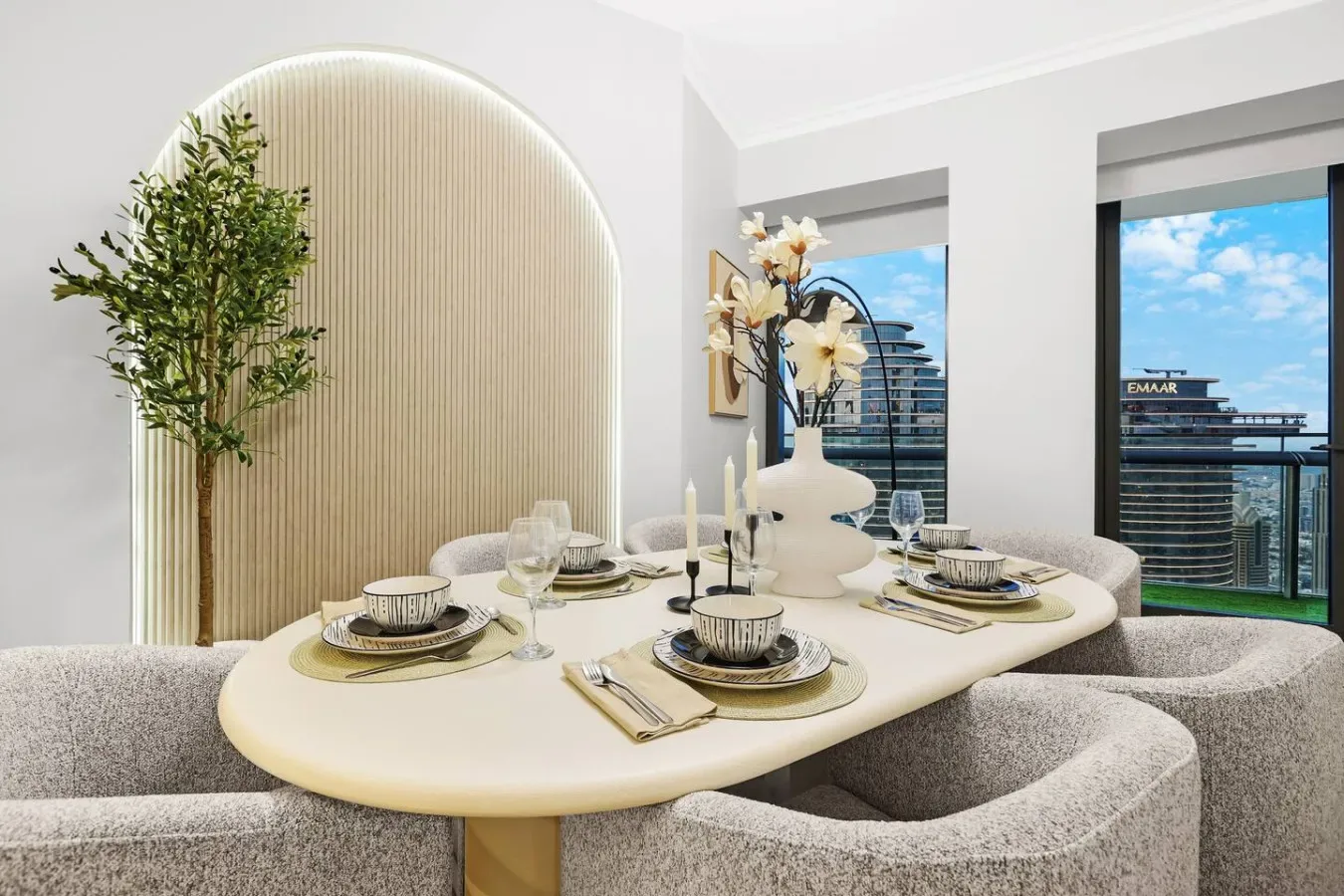 Un comedor cuenta con una mesa puesta junto a grandes ventanas con vistas a edificios de la ciudad.