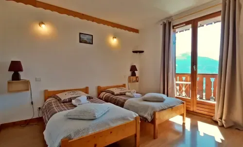 Habitación con dos camas individuales de madera y balcón con vistas a las montañas