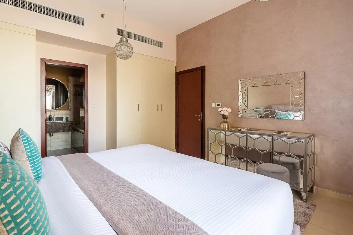 Un dormitorio con una cama bien tendida, una cómoda con espejo y una puerta al baño.