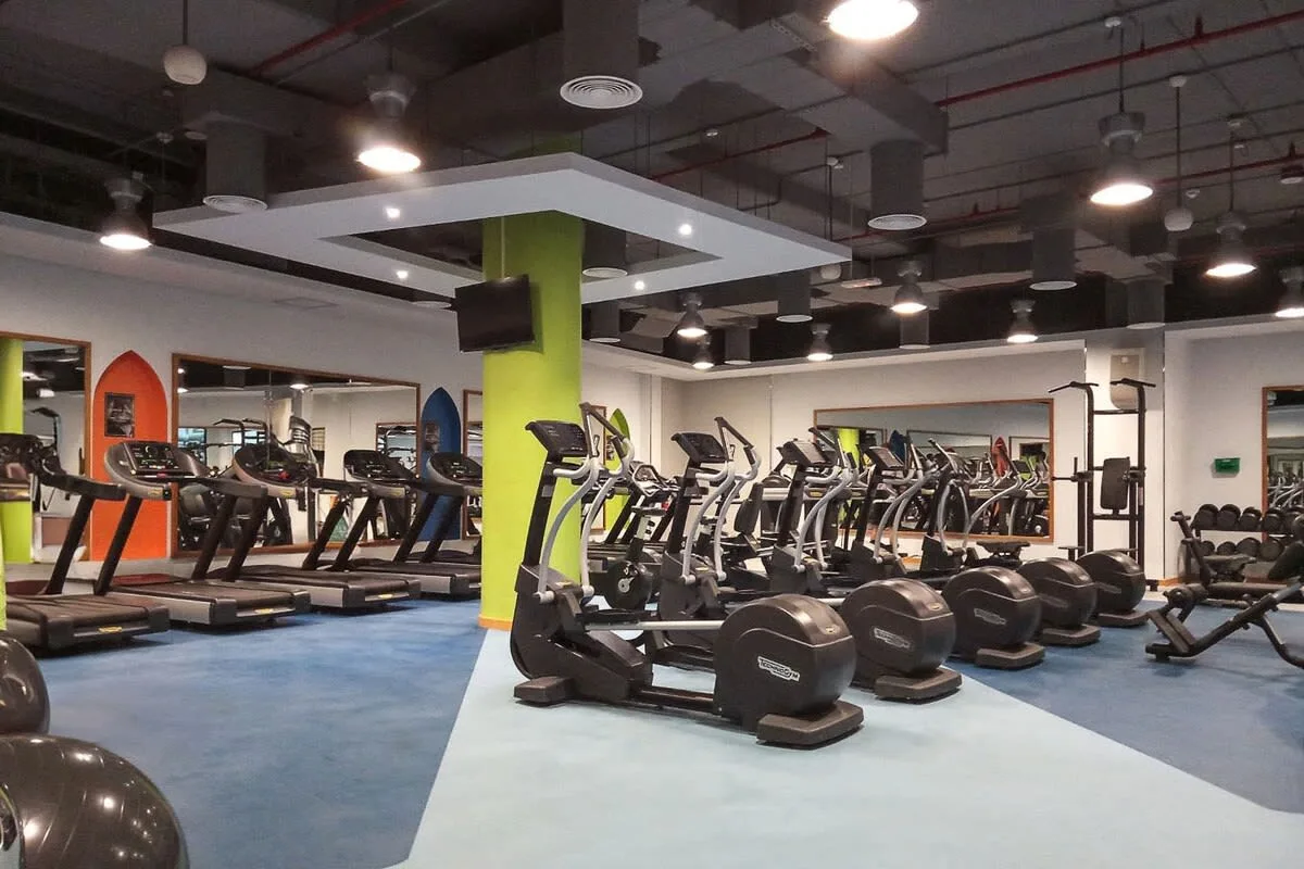 Un gimnasio con filas de cintas de correr y equipos de entrenamiento con pesas.