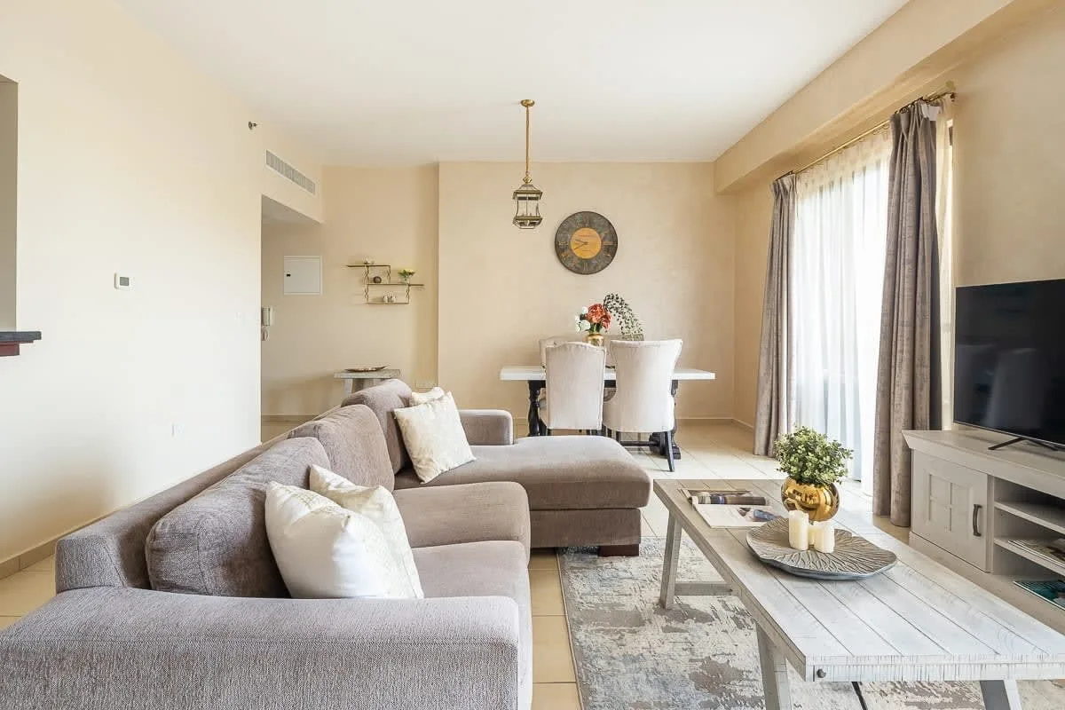 Una sala luminosa con asientos seccionales, una mesa de centro y grandes ventanas con cortinas.