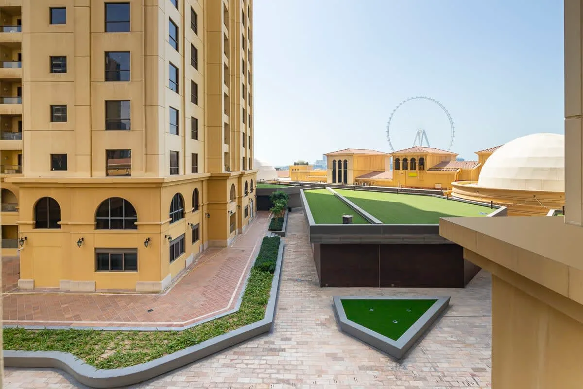 Un patio pavimentado entre edificios beige cuenta con senderos ajardinados y una terraza en la azotea.