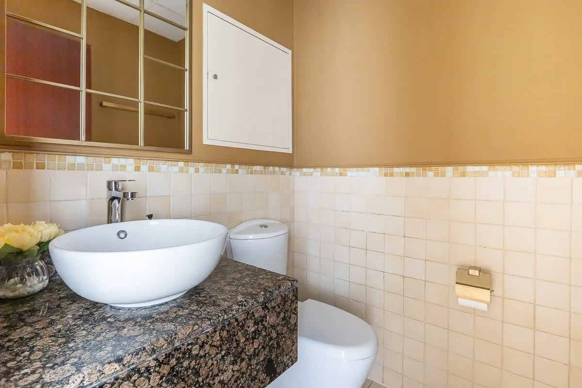 Un baño con un lavabo sobre una encimera con patrón de piedra y paredes revestidas de azulejos.