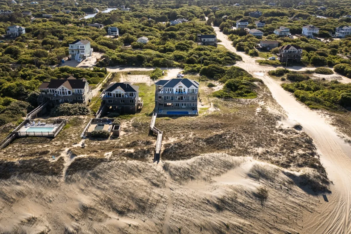 An aerial view of houses among low vegetation beside sandy roads.