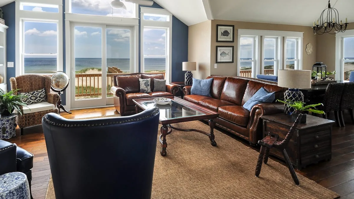 A living room with seating arranged around a coffee table beside large windows.