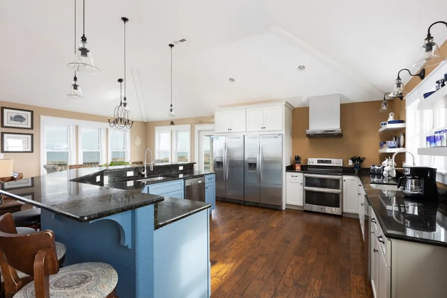 A spacious kitchen with dark countertops, stainless steel appliances, and wooden flooring.