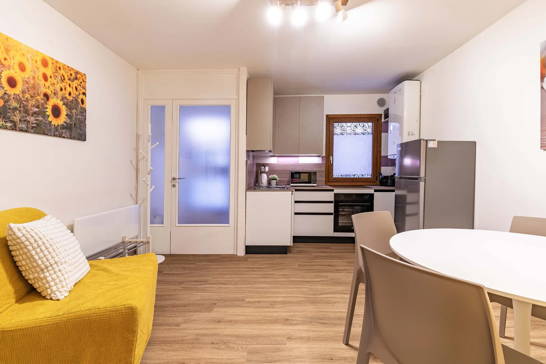 Sala de estar y cocina de concepto abierto, con un sofá amarillo y una mesa de comedor.