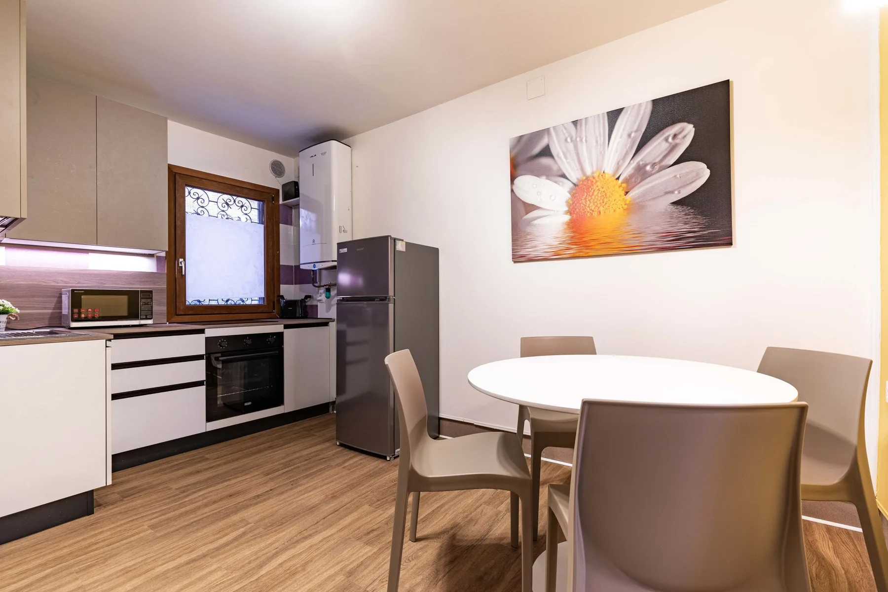 A kitchen and dining area with a round table and flower artwork on the wall.