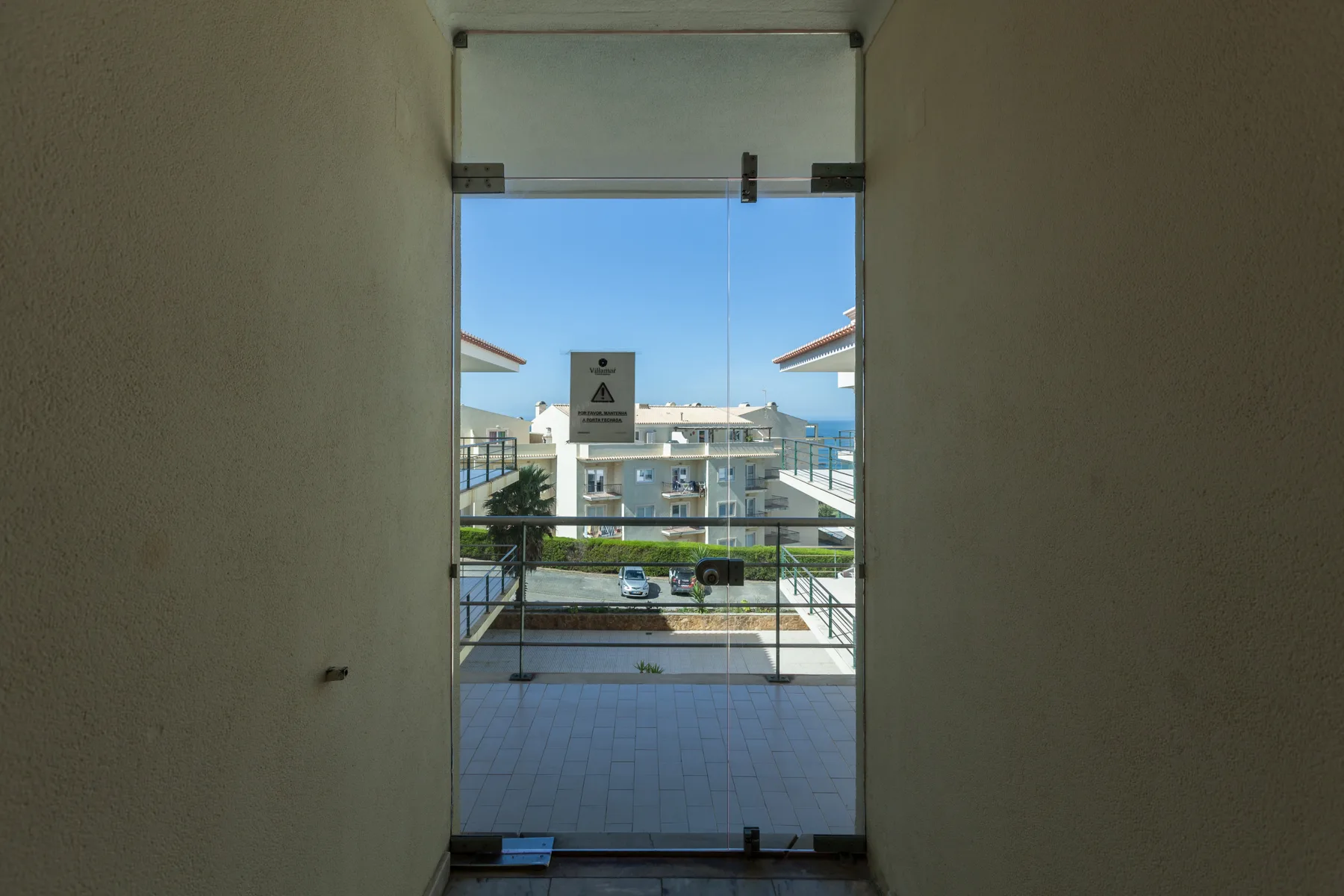 A balcony doorway opens onto a tiled terrace with a view of the sea.