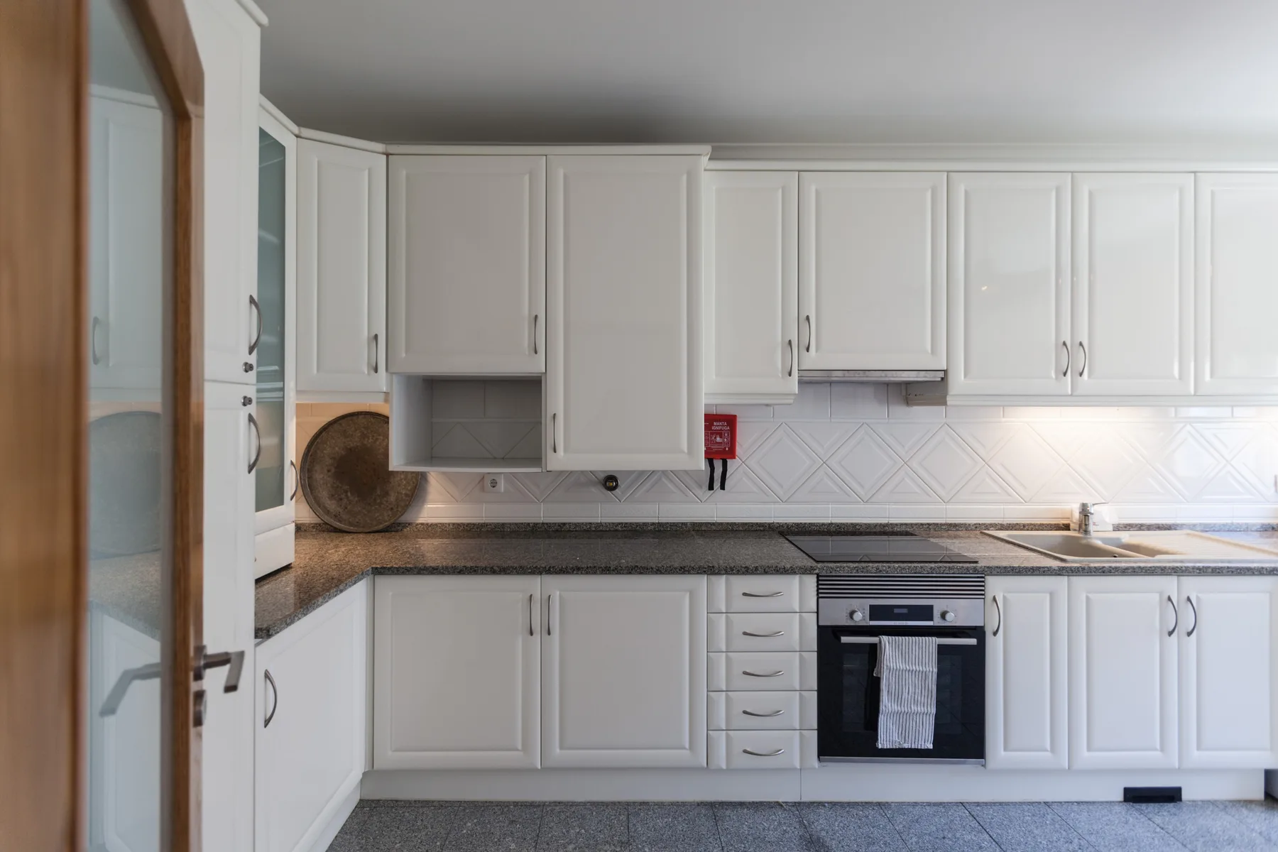 A bright kitchen with white cabinets, dark countertops, and an oven.