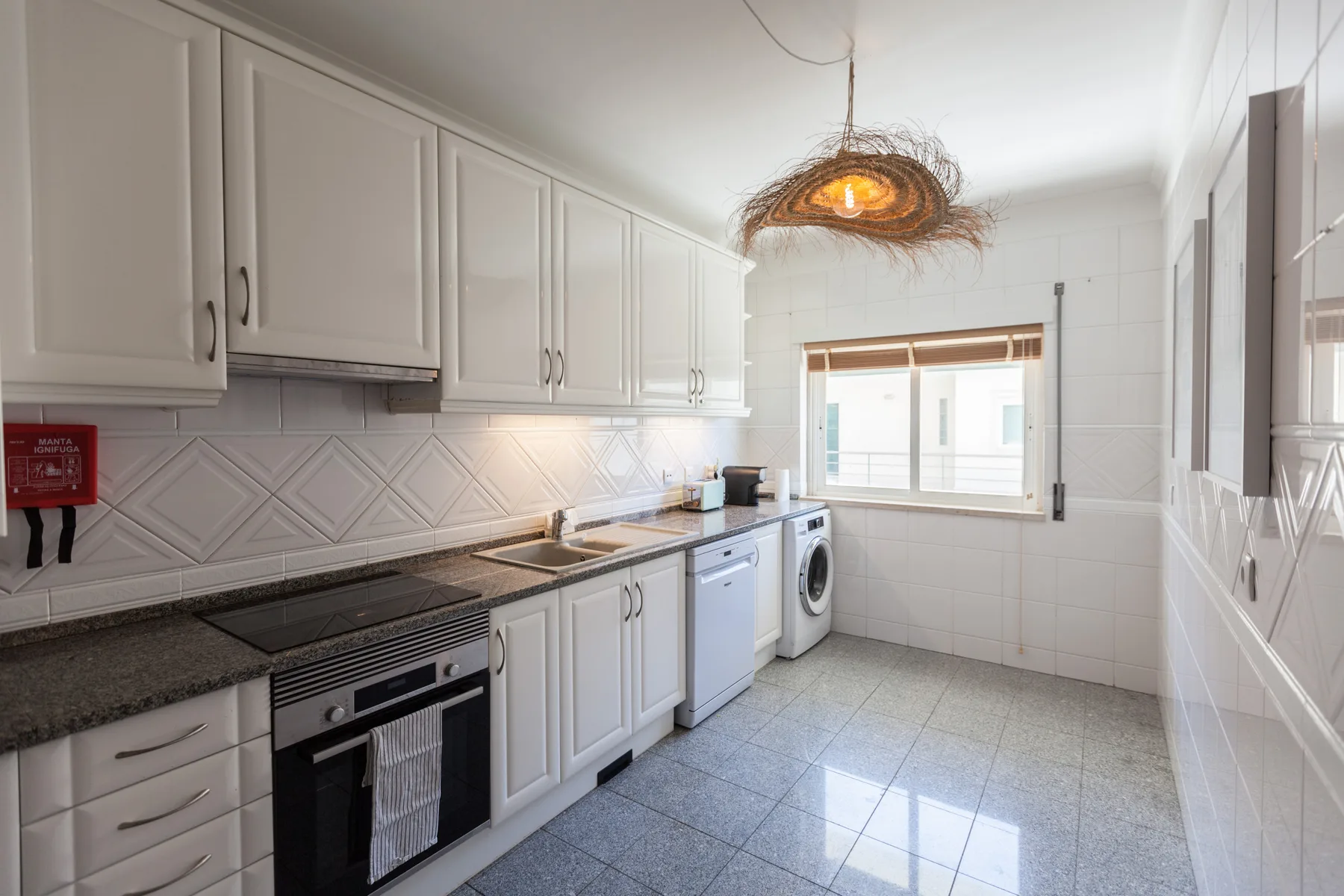 A bright kitchen with white cabinets, dark countertops, and a window.