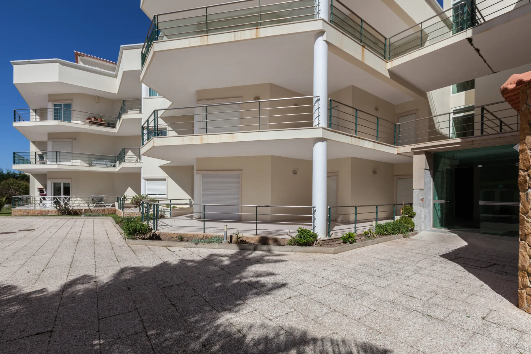 Exterior view of a modern apartment building with balconies and a paved courtyard.