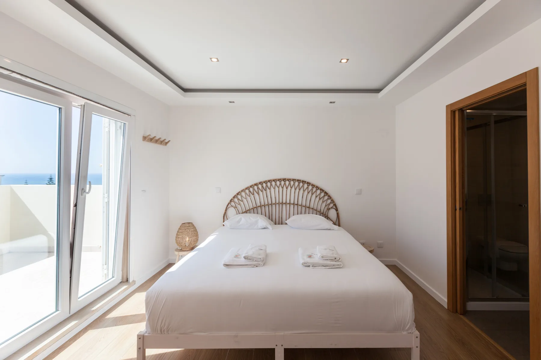 A bright bedroom with a bed beside a glass door opening onto a balcony.