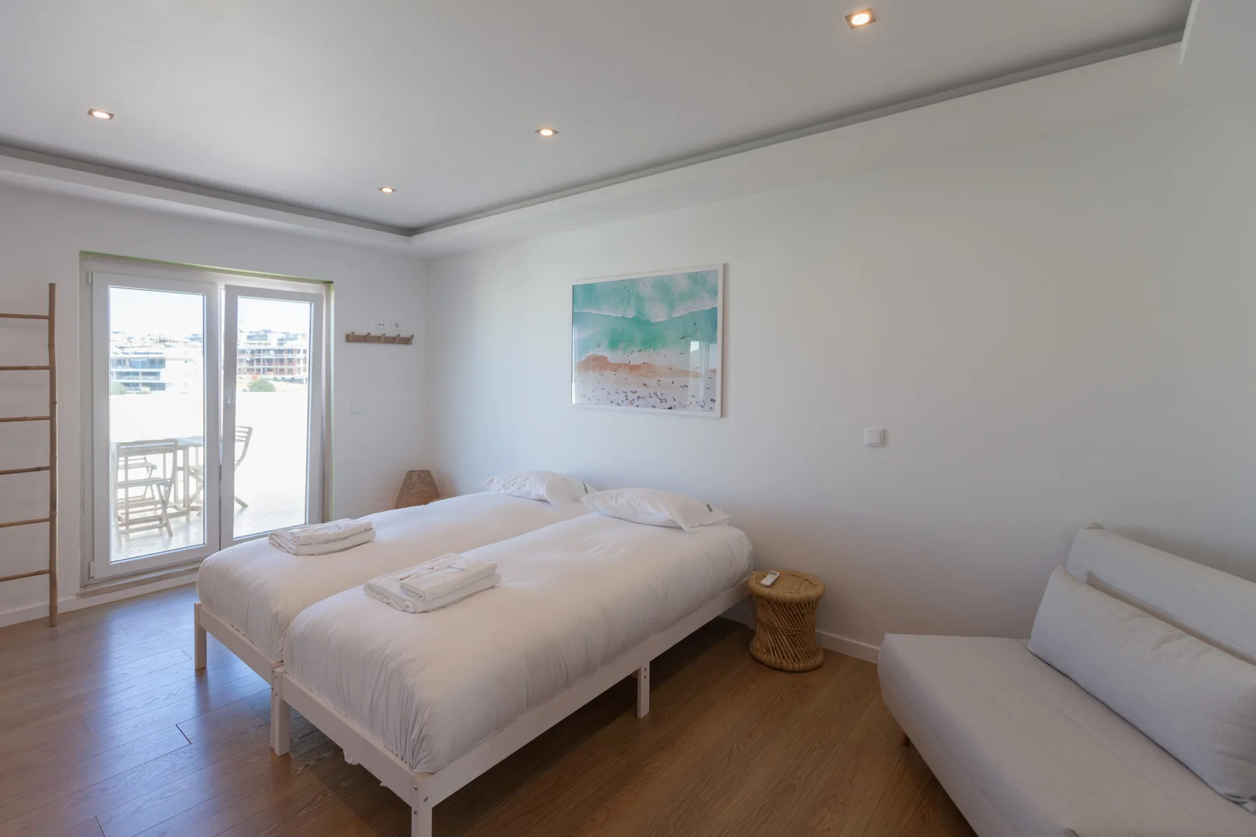 A bright bedroom with a bed, a seating area, and glass doors opening to a balcony.