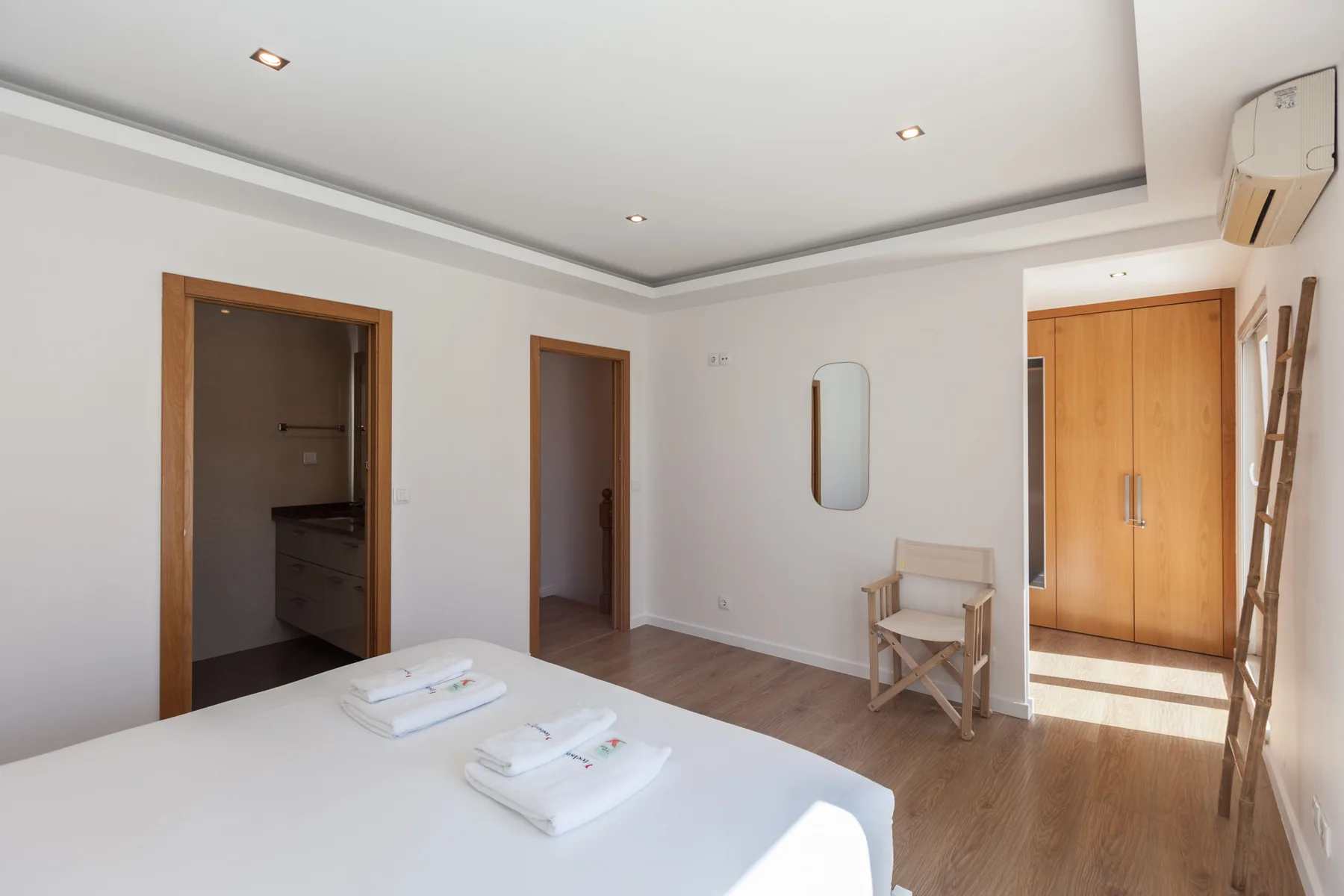 A bright bedroom with a bed, wooden doors, and a small chair.