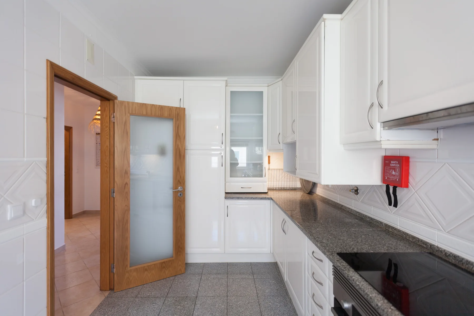A bright kitchen with white cabinets, dark countertops, and a wooden doorway.