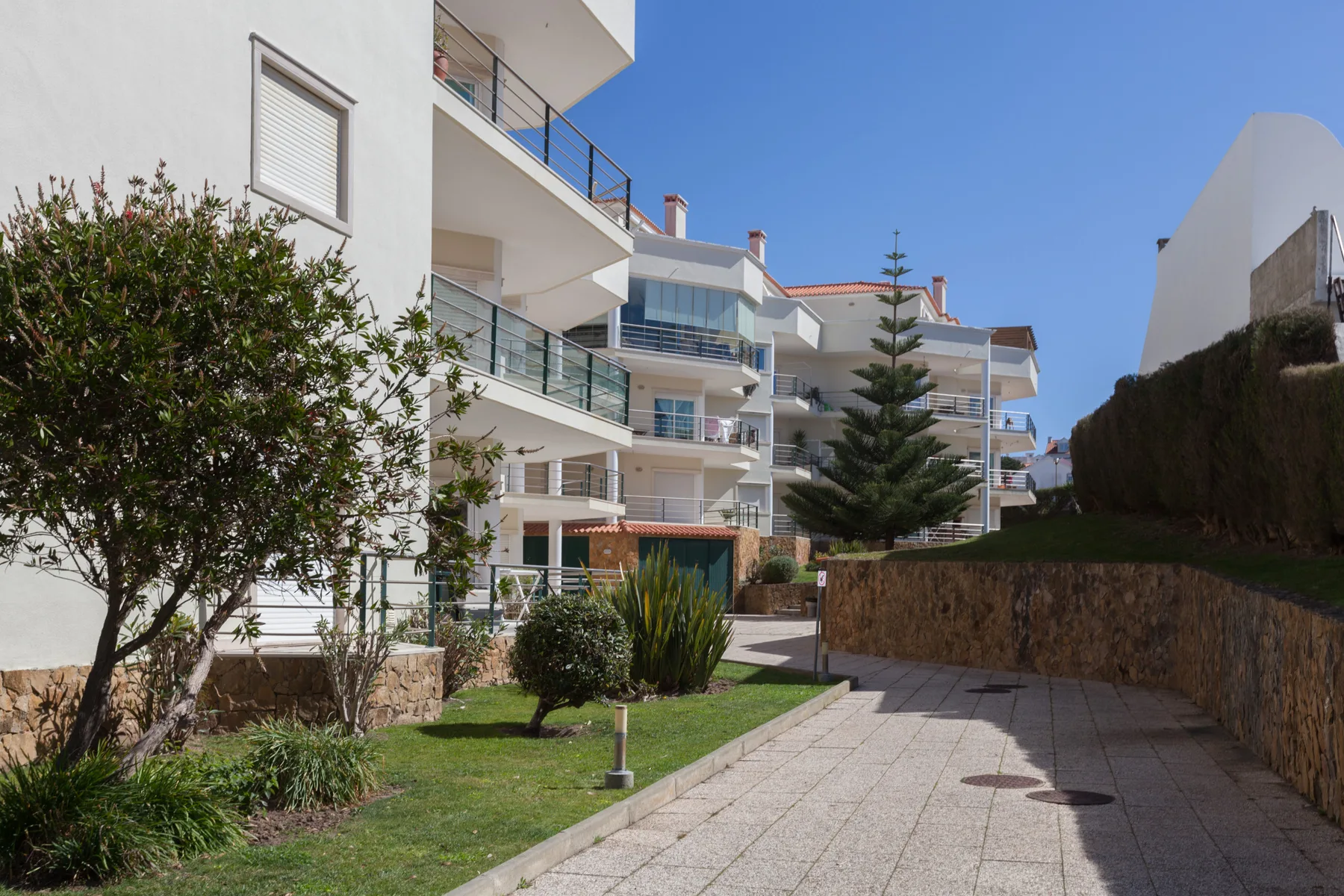 Apartment buildings overlook a paved walkway beside a small landscaped lawn.