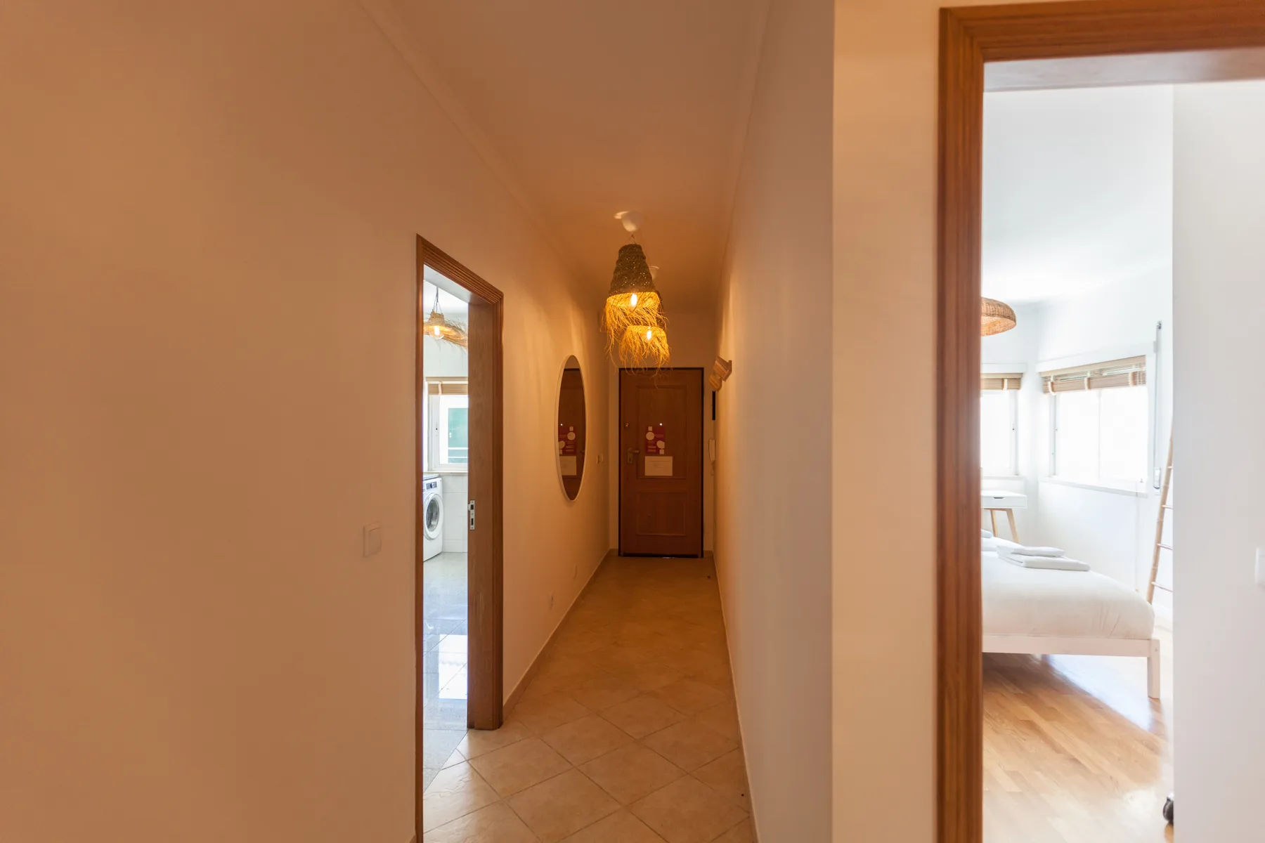 A narrow hallway leads to a bedroom with a bed and bright windows.