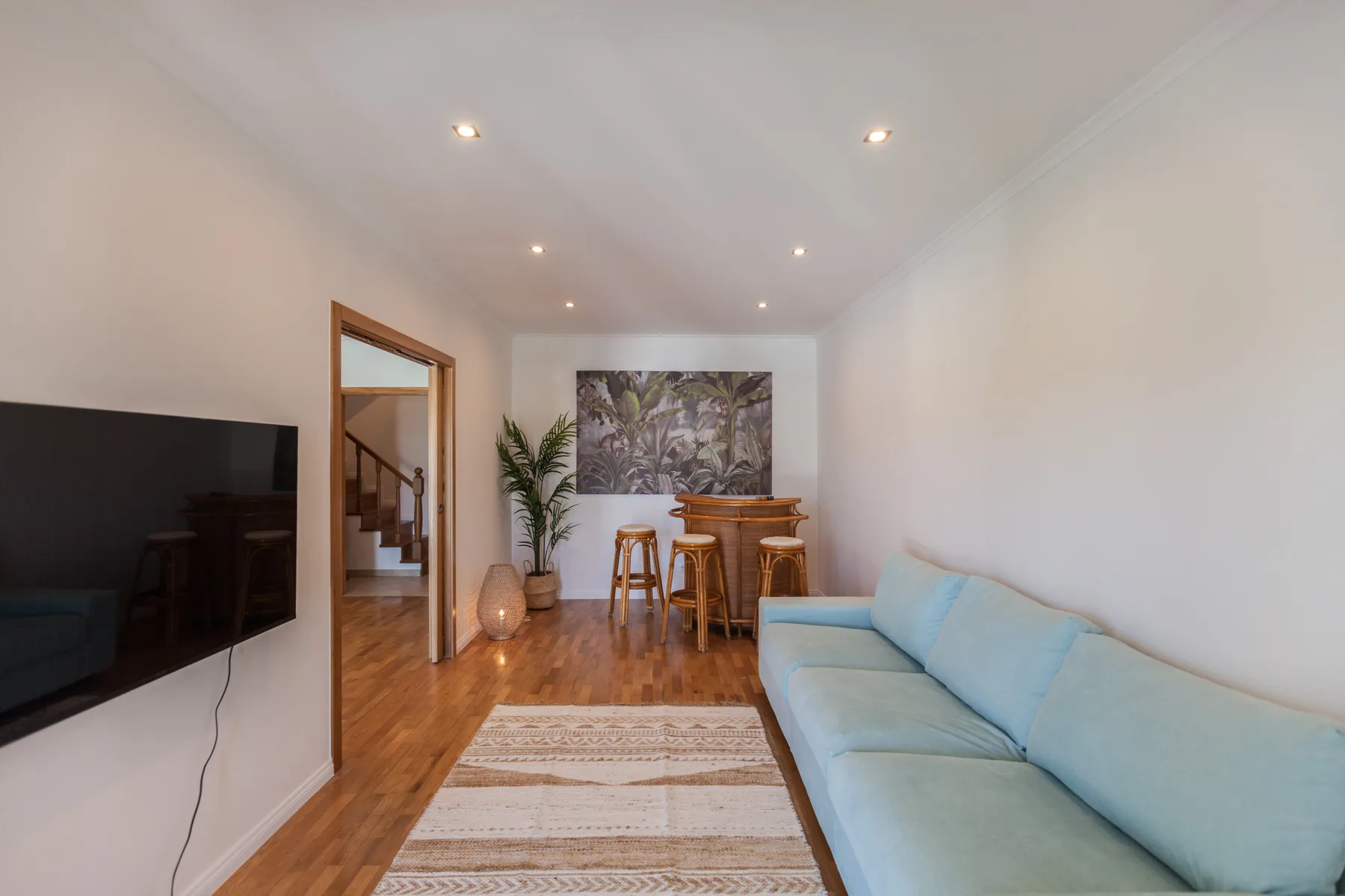 A bright living room with pale blue seating, a television, and a dining area.