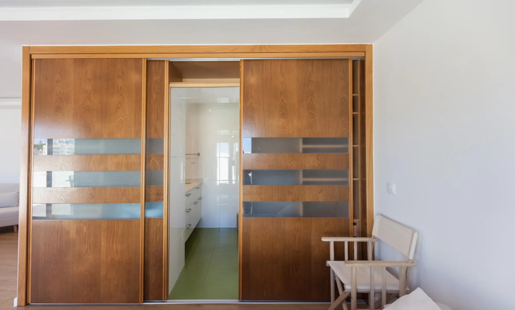 A bedroom with wooden sliding doors opening onto a bright adjoining room.