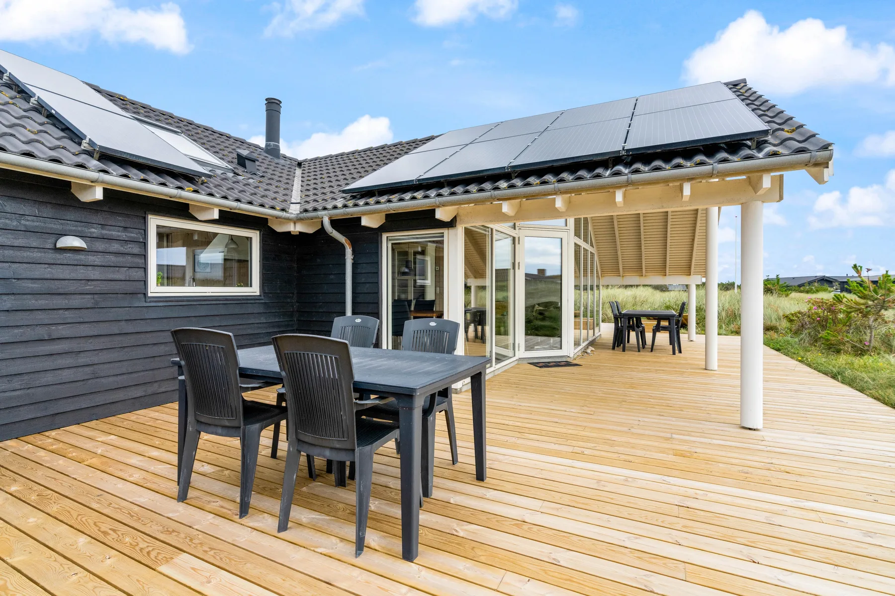 Una terraza de madera con asientos para comer al aire libre junto a una casa oscura.