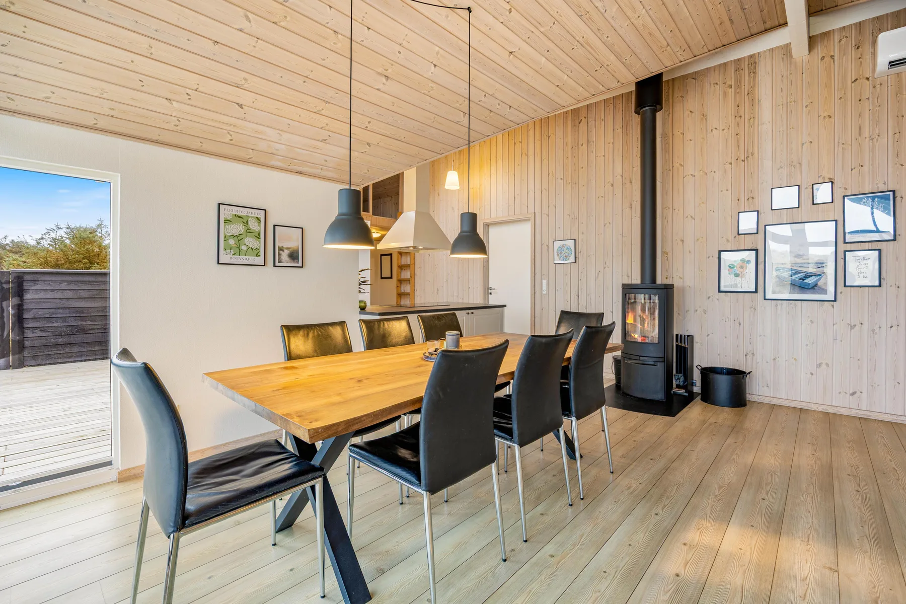 Un comedor con una mesa de madera, asientos oscuros y lámparas colgantes.