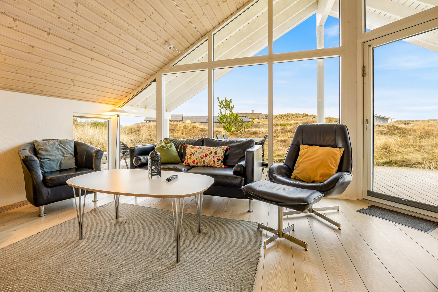 Una sala luminosa con asientos junto a grandes ventanales con vistas a las dunas.