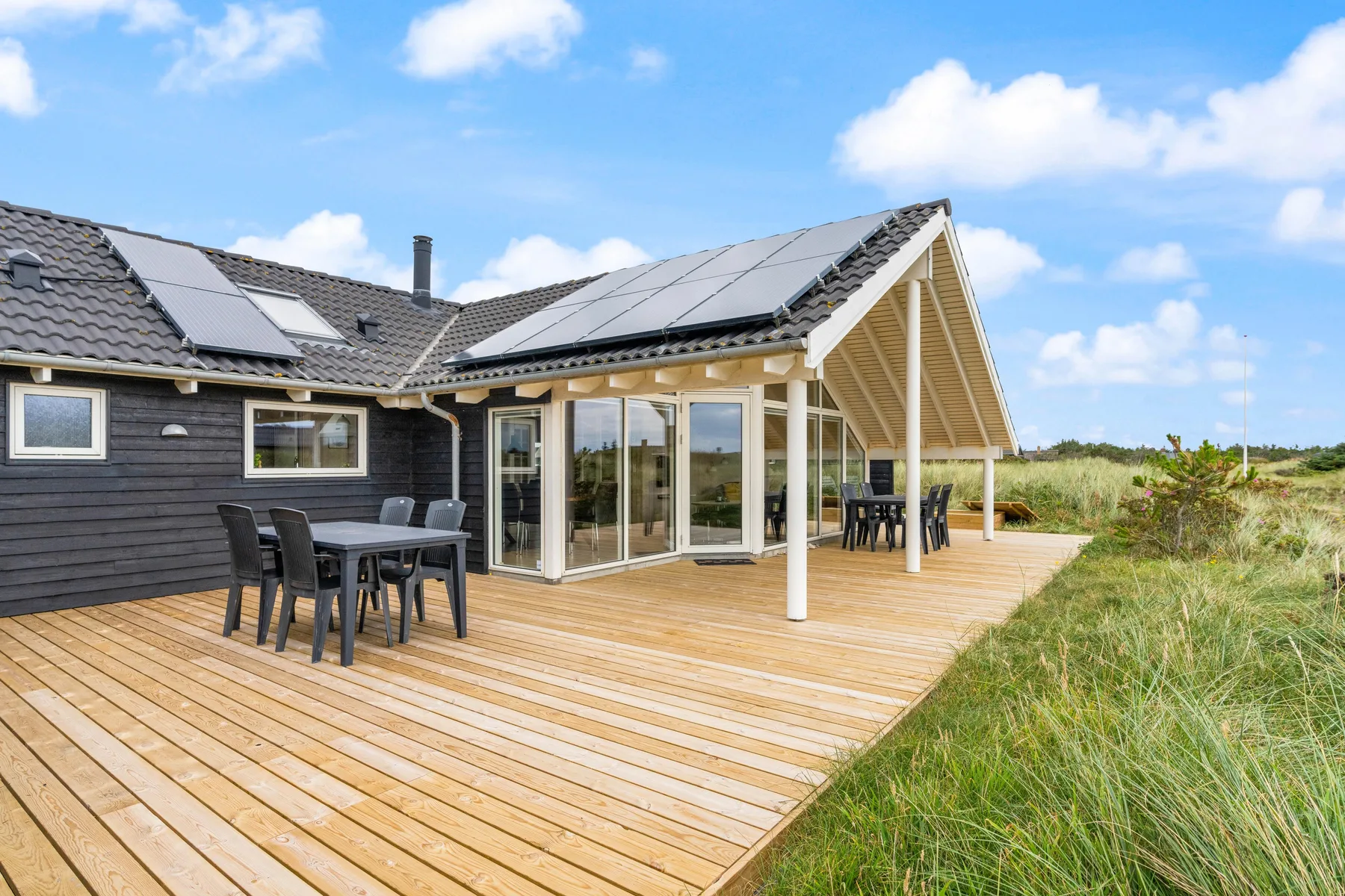 Una casa moderna se abre a una terraza de madera con muebles para comer al aire libre.