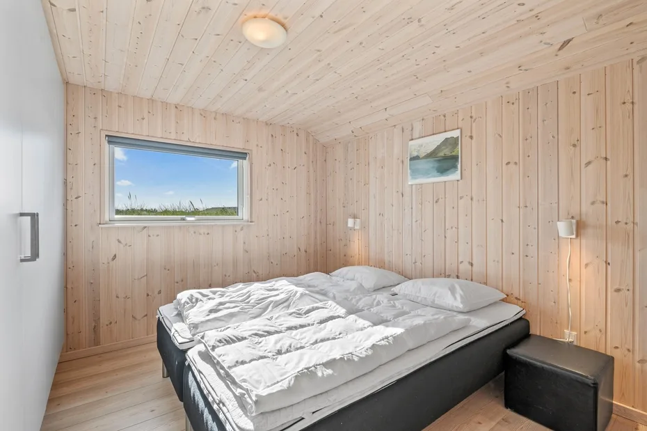 Un dormitorio con una cama, paredes revestidas de madera clara y una ventana.