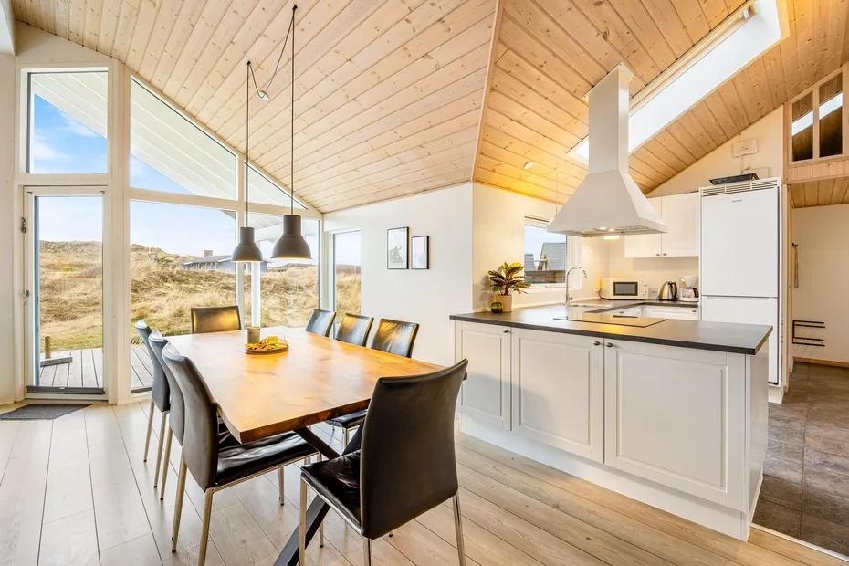 Una cocina abierta y comedor cuentan con una mesa larga junto a grandes ventanas.