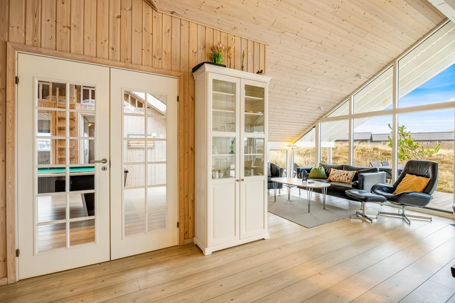 Una luminosa sala revestida de madera, con puertas acristaladas, una vitrina y asientos junto a grandes ventanas.