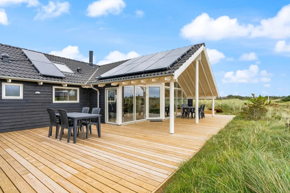 Una casa moderna da a una amplia terraza de madera con asientos al aire libre y puertas de vidrio.